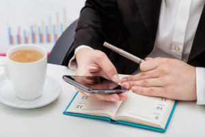 Businesswoman on her smartphone with a day planner and pen